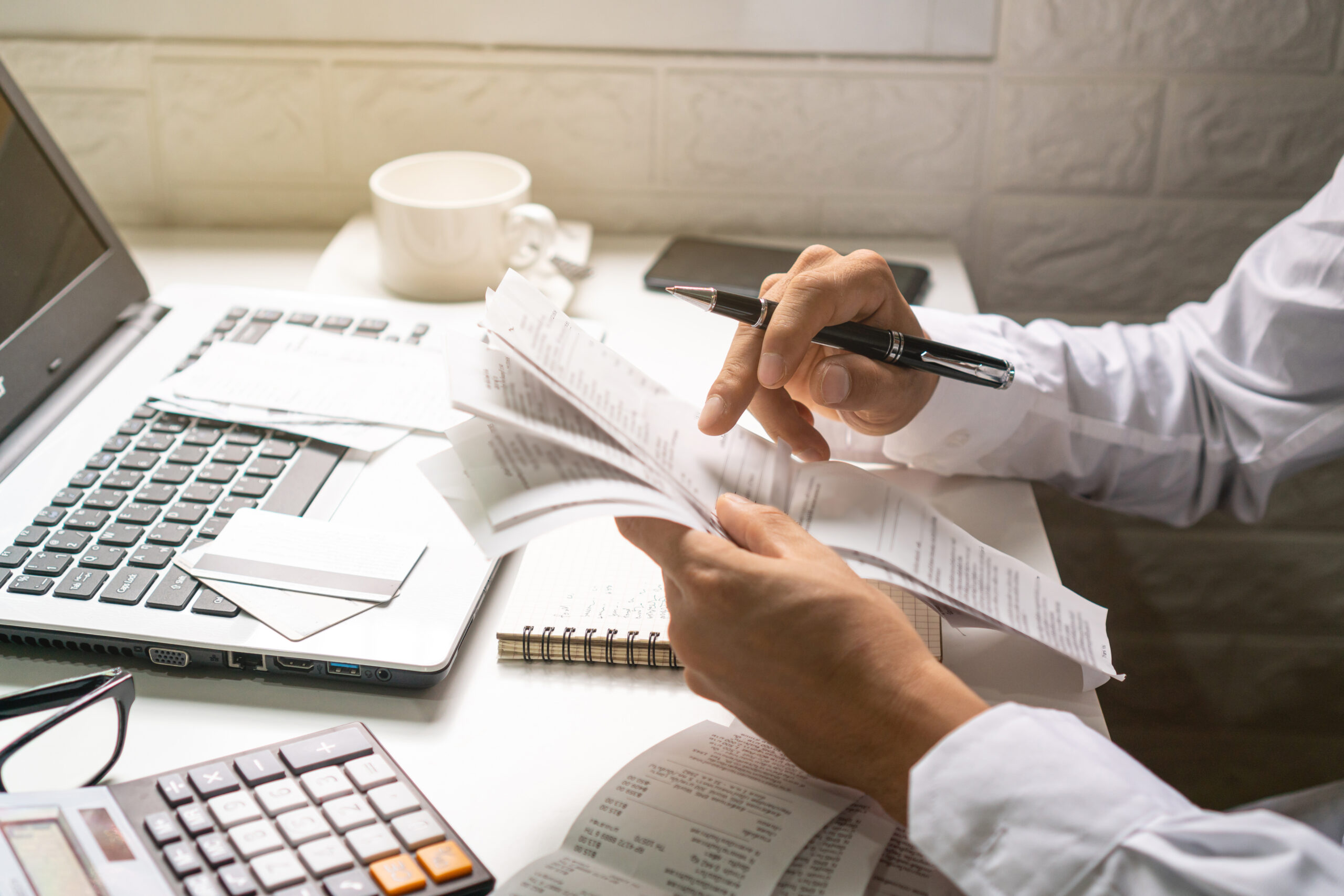 A business man holding pen while looking at the bills in his workplace. Business concept.